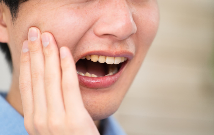 親知らずが横向きに生えて違和感を感じ頬を押さえる男性