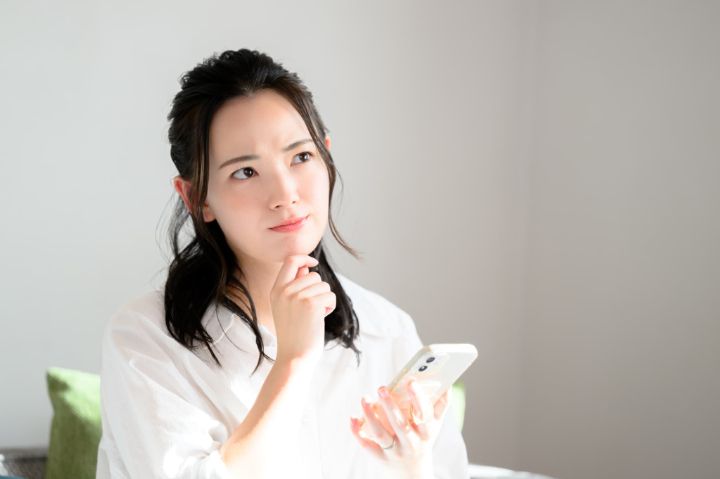 横向きに生えた親知らずは抜歯したほうがよいかスマホで調べる女性