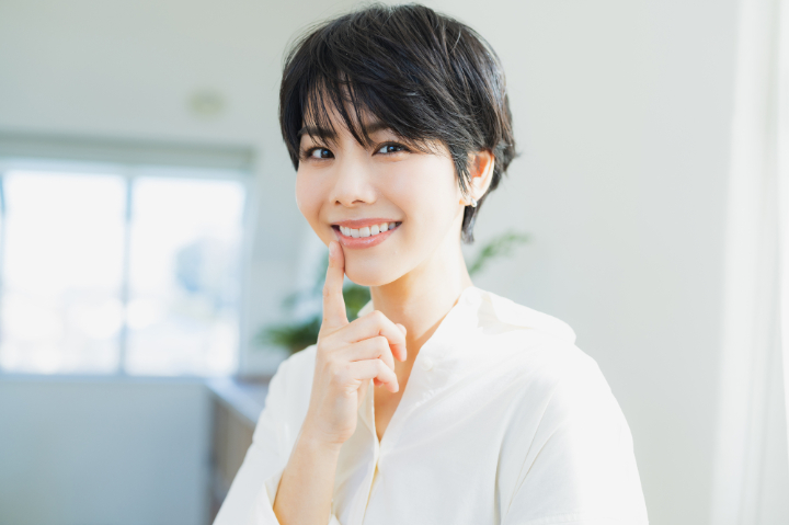 白い歯を指さして笑顔を見せる女性